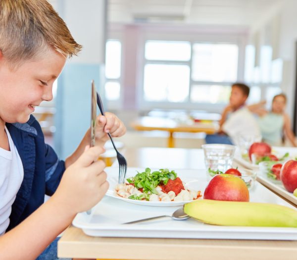 Happy,Schoolboy,Eating,Meal,With,Cutlery,While,Sitting,At,Table
